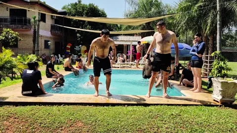 Young men taking turns performing jumps and tricks into swimming pool during 스톡 동영상 331269026