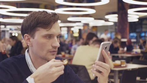 Young men using smartphone eat fried chicken wings at food court in shopping Stock Footage 70149804