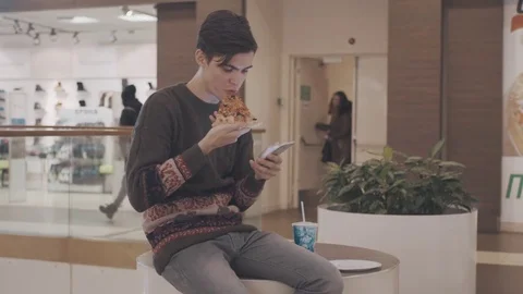 Young men using smartphone eat pizza and drink coke at shopping mall Stock Footage 70188175