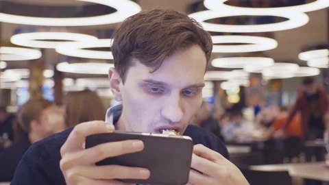 Young men using smartphone eat Shawarma roll at food court in shopping mall Video stock 70188307