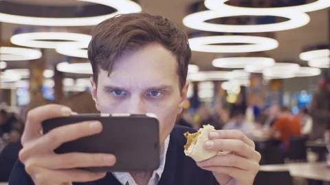 Young men using smartphone eat Shawarma roll at food court in shopping mall Stock Footage 70188804