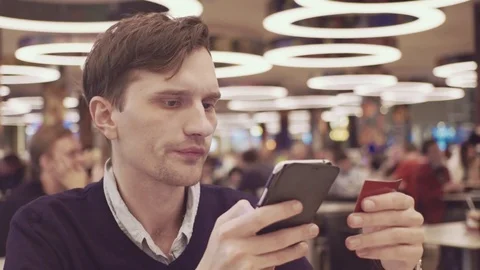 Young men using smartphone putting promo-code at food court in shopping mall Video stock 70188809