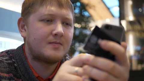 Young men using smartphone putting promo-code at food court in shopping mall. A Stock Footage 82331031