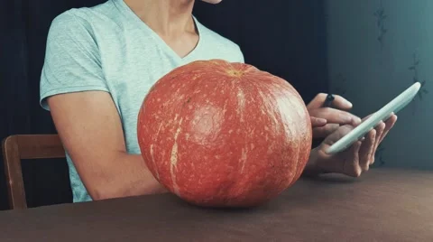 Young men in white t-shirt use tablet computer and examine pumpkin in front of Stock Footage 68302279