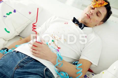 Young messy man sleeping at party with piece of pizza on his forehead Stock Photos