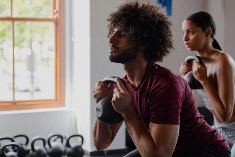 Young middle eastern man and biracial woman doing kettlebell squats at the gym Stock Photos