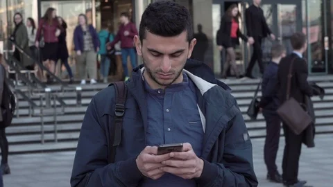 Young middle eastern man using smartphone in city, people are walking behind Stock Footage 88773294