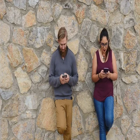 Young Millenial couple against rock wall laughing and texting Stock Footage