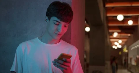 Young Millenial Guy in White T shirt Using his Smartphone, Smiling and Saying Stock Footage 119058937