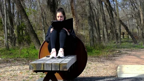 Young millennial lady sitting alone outside on park bench reading a tablet Vídeo Stock 134424852