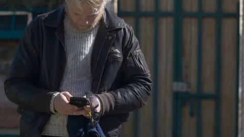 A young millennial man texting on his cell phone outside wearing a jacket Stock Footage 72363917