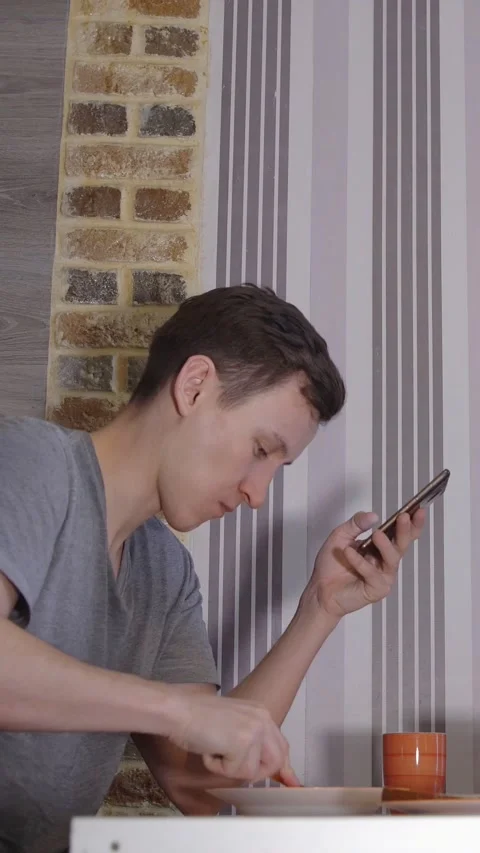 Young millennial man using smartphone while eating breakfast in the kitchen Video stock 341679071
