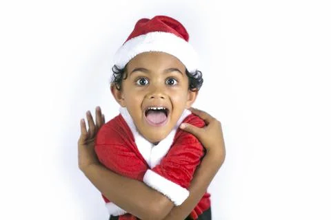 A young mixed race boy in a red Santa's outfit hugs himself and screams Stock Photos