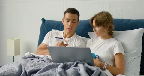 Young mixed race couple is doing online shopping, lying in a bed Stock Footage 114642482