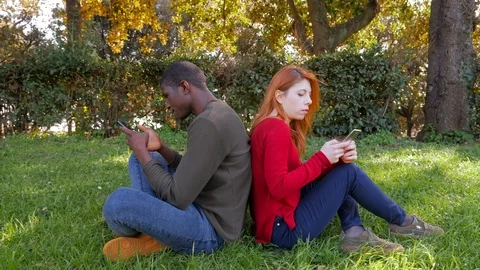 Young mixed race lovers focused on own smartphones in the park.technology, youth Stock Footage 112279712
