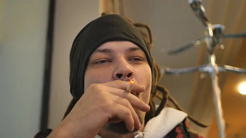 A young mixed race man with dreadlocks emits smoke rings while smoking a cigaret Stock Footage 222796238