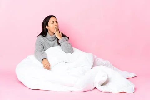 Young mixed race woman wearing pijama sitting on the floor yawning and coveri Stock Photos