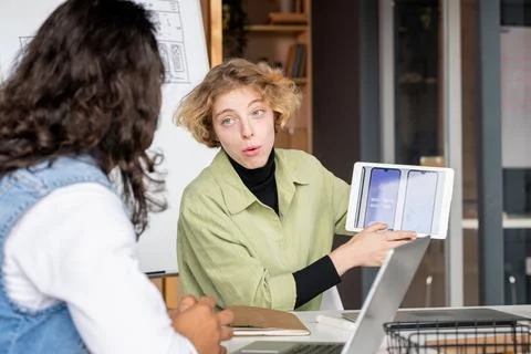 Young mobile app developer presenting colleague some new ideas on tablet display Stock Photos