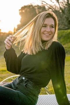 Young model dressed in black touching her blonde hair while smiling and looki Stock Photos