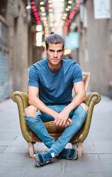 Young model seated on couch looking at camera for social media or dating apps - Stock Photos