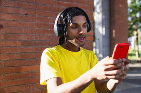 Young modern black guy with helmets smiling and checking his cell phone in .. Foto stock