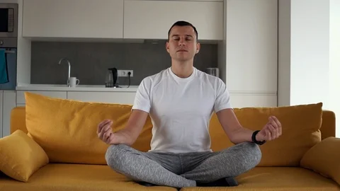 Young modern caucasian man practice yoga lotus pose sitting on a yellow couch Stock Footage 124879150