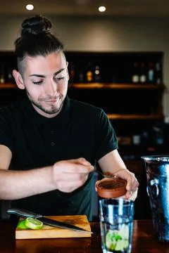 Young, modern waiter, adding brown sugar in a large crystal glass to prepare a Stock Photos