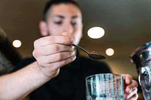 Young, modern waiter, adding brown sugar in a large crystal glass to prepare a Stock Photos