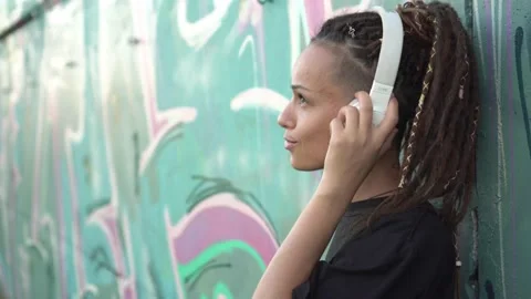 Young modern woman listens to music on headphones outdoors against the Stock Footage