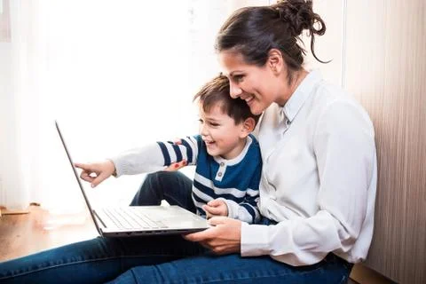 Young mom and her son, sitting on the floor looking at laptop. Video call Stock Photos