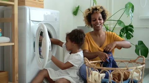 Young mom and laundry wash machine cloth, little daughter loading washing Video stock 140875841