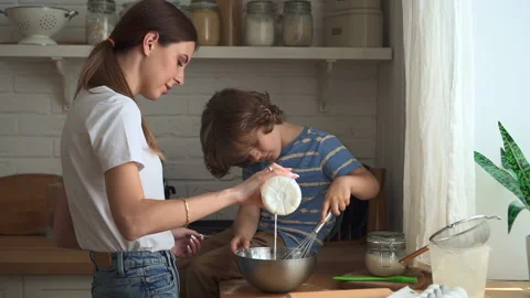 Young mom and son making dough and standing in home kitchen indoors. Video stock 158980005