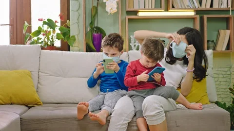 Young mom with her two sons on the sofa wearing the protective mask while is Video stock 127708022