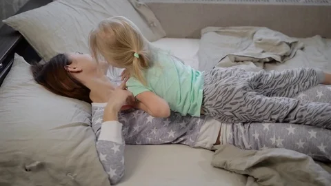 Young mother and her daughter lying in bed and fool around with each other in Stock Footage