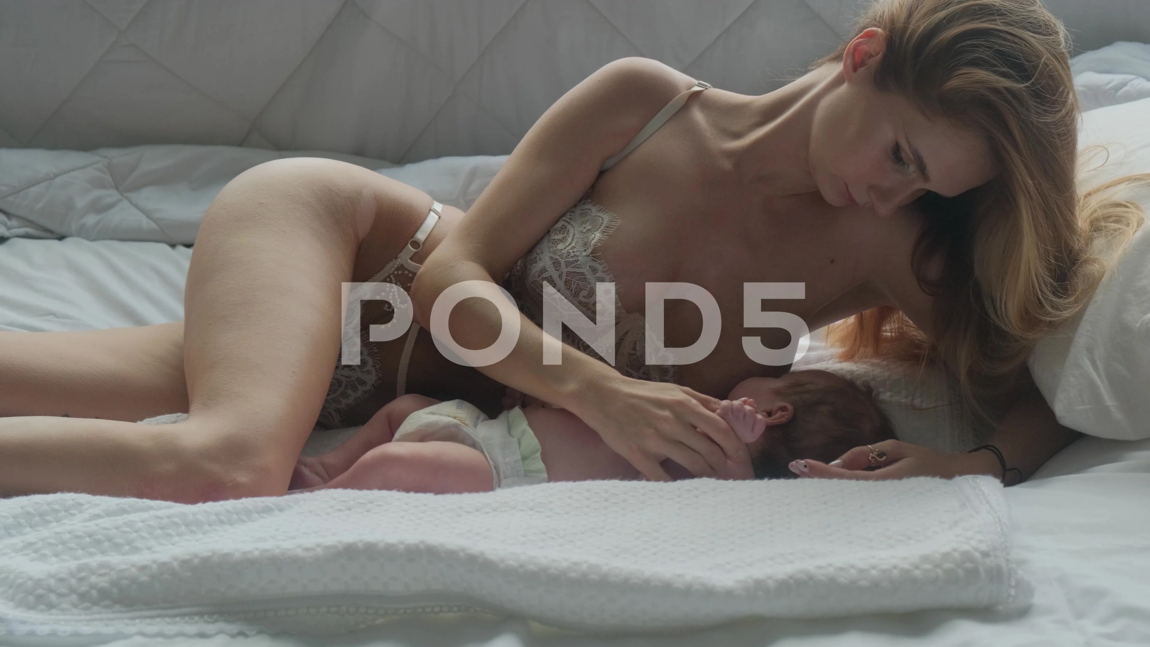 Young mother breastfeeding her baby on the bed at home in a white room