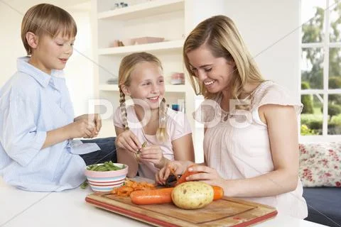 Young mother with children peeling vegetables in kitchen Stock Photos