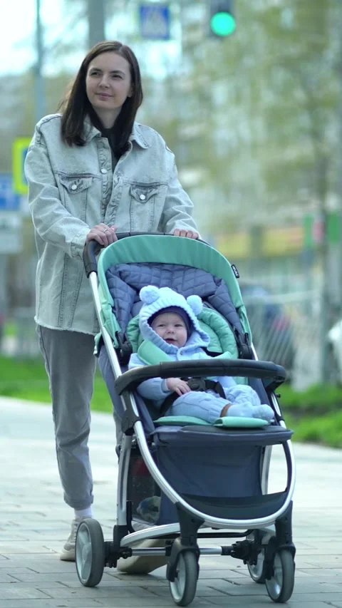 Young mother in denim jacket pushes mint stroller with smiling baby Stock Footage 341530277