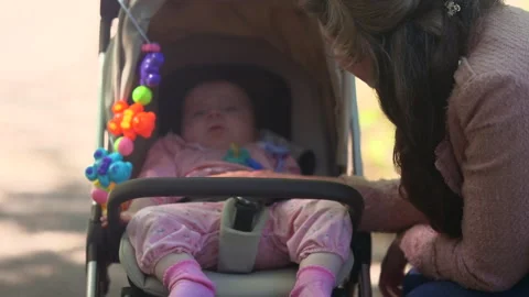Young mother gently interacting with her infant seated in a stroller during an 動画素材 336937585