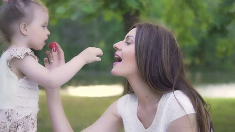 A young mother with a little daughter are feeding each other a strawberry in the Stock Footage