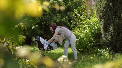 Young mother lovingly picking up her baby from a stroller outdoors 動画素材 338367717