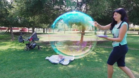 Young mother making soap bubbles in the park, slow motion. Stock Footage 102598871