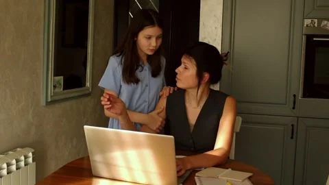 Young mother manages remote work at kitchen table as her daughter leans Stock Footage 307872015