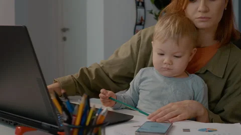 Young mother multitasks with baby while shopping online from home office Stock Footage 302912729