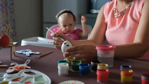 Young mother painting Easter egg while her baby playing Stock Footage 263835591