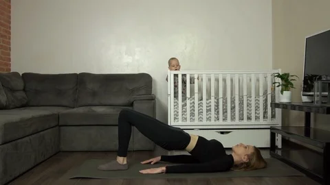 Young mother performs an exercise at home. Baby on the background. Dolly shot Video stock 124434083