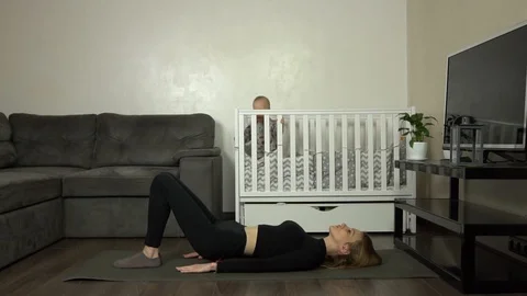 Young mother performs an exercise at home. Baby on the background. Slow motion Stock Footage 124434085