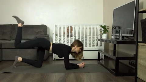 Young mother performs an exercise at home. Baby on the background. Slow motion Stock Footage 124434135