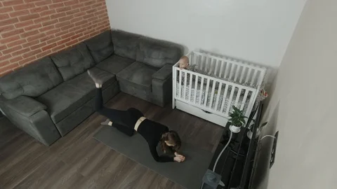 Young mother performs an exercise at home. Baby on the background. Stock Footage 124434206