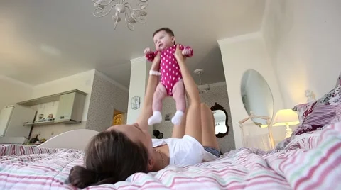 Young mother playing with her little baby on the bed - indoors Stock Footage