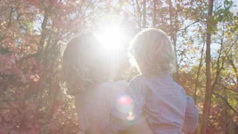 Young mother points up to tree leaves and toddler holding stick raises arm Video stock 194460707
